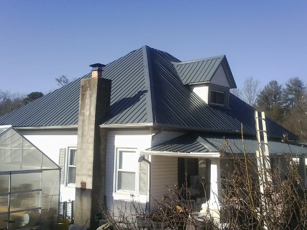 Dark blue standing seam metal roof on a white farmhouse with dormer — Slate & Tile Roof Repair by Roofing Brothers in Horicon