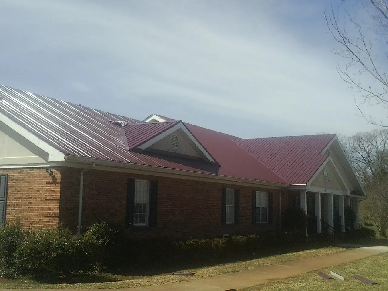 Red metal roof with gabled entries on a long brick building, from a Hail Damage Roof Repair job in Horicon
