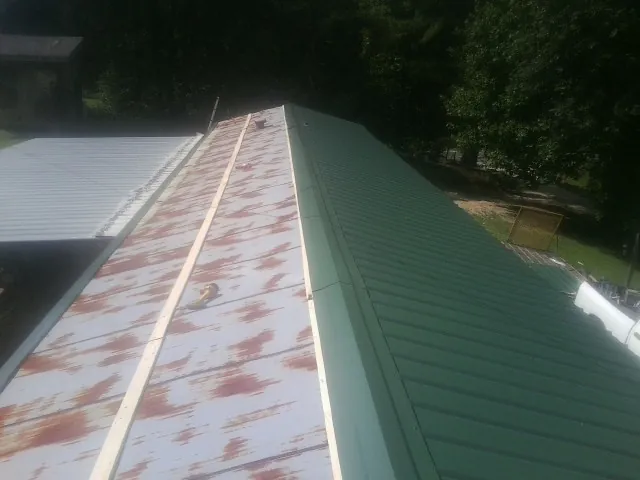 Old rusted panels beside newly installed green metal roofing — Wind Damage Roof Repair by Roofing Brothers in Horicon