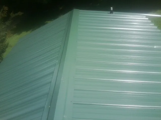 New green metal panels meeting at the ridge of a roof — Flat Roof Repair work by our crew in Horicon