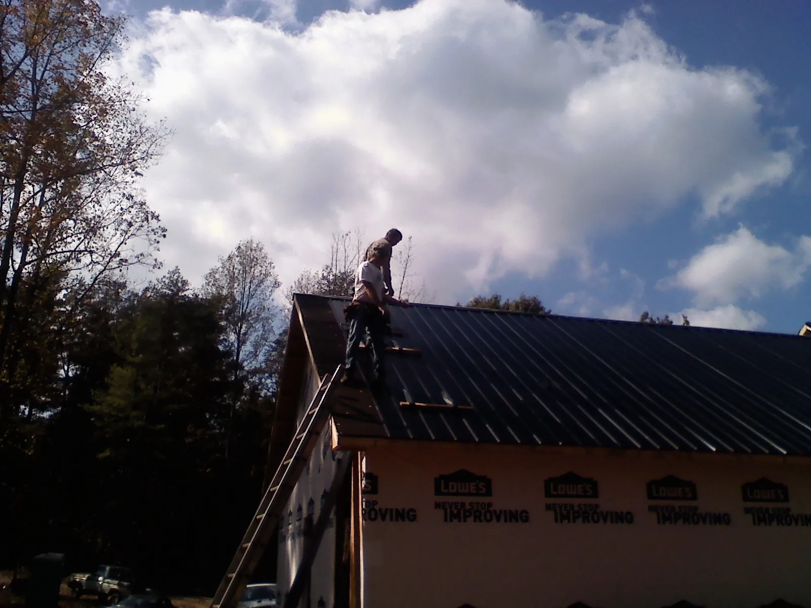 Roofer fastening dark metal panels high against a cloudy sky, from a Roof Inspection job in Horicon