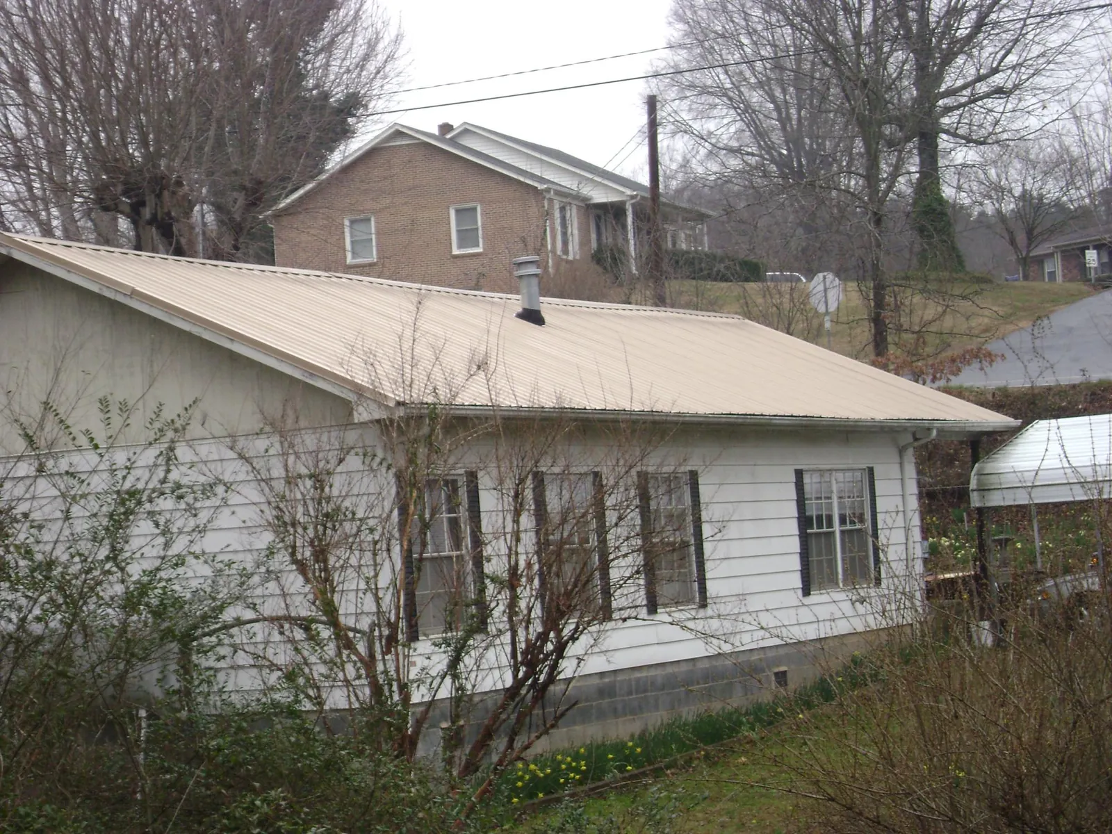 Tan metal roof on a white sided house set into a hillside — Commercial Roofing by Roofing Brothers in Horicon