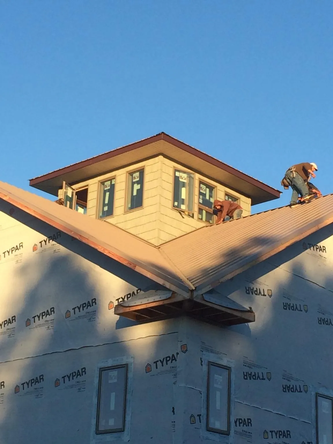 Roofers working around a rooftop cupola on a new metal roof at sunset — Roof Waterproofing in Horicon by Roofing Brothers